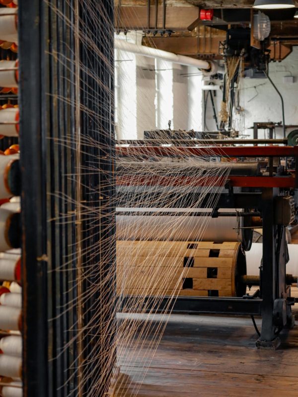 pexels-photo-16176408-16176408 View inside a spinning mill with threads on machinery, showcasing modern textile production.